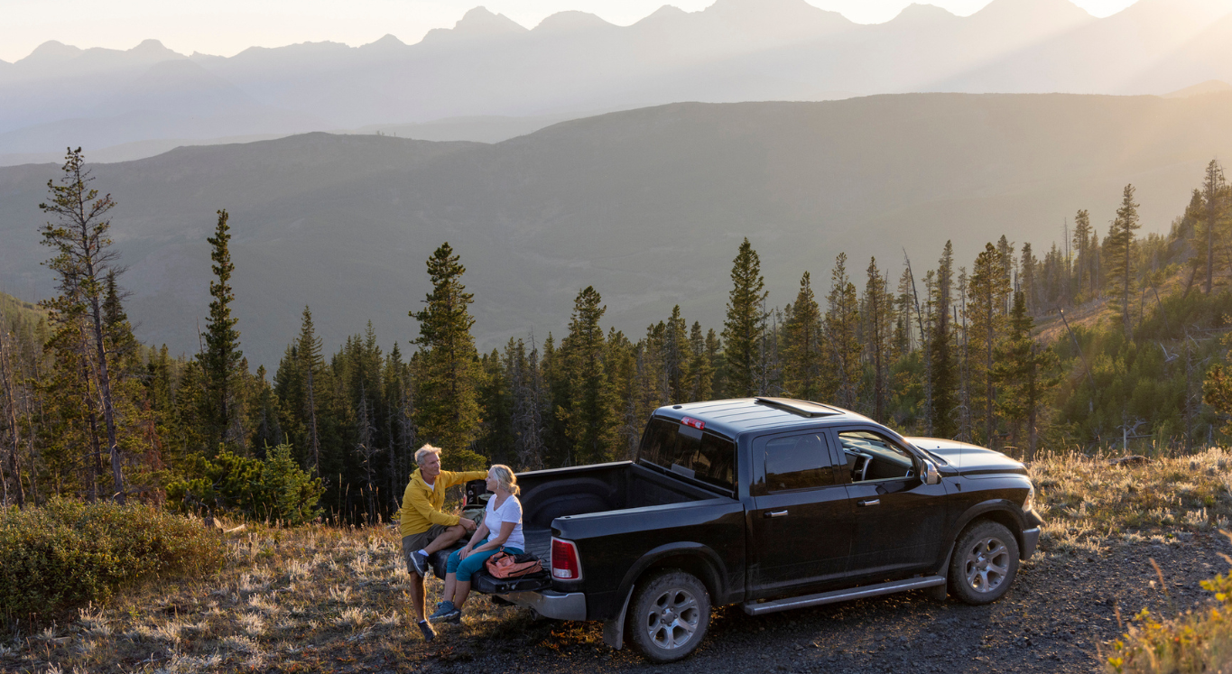 Couple sitting on edge of truck bed near mountains